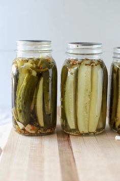 three jars filled with pickles sitting on top of a wooden table