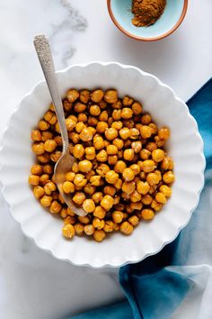 a white bowl filled with chickpeas next to a blue napkin and a spoon