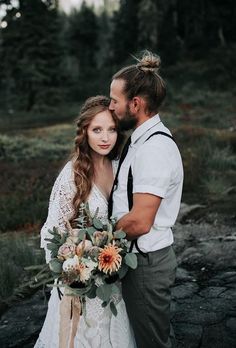 a bride and groom standing together in the woods