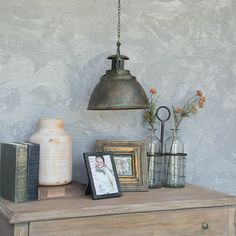 a lamp hanging over a dresser with pictures and vases sitting on top of it