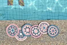 four circular crocheted coasters sitting next to a swimming pool with water in the background