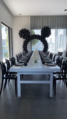 a long table with black chairs and mickey mouse balloons on the wall above it, in front of a large window