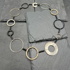 Rings of various sizes, textures and thicknesses are crafted in sterling silver, gold-fill and black rubber to create this one-of-a-kind necklace. 18 inches in total length. Handcrafted in Boulder, CO. Black Metal Circle Necklaces, Black Circle Metal Necklaces, Black Metal Circle Necklace, Black Metal Circular Necklace, Black Circular Metal Necklace, Elegant Black Hand Forged Necklace, Gold Necklaces With Sterling Silver Clasp, Modern Gold Necklace With Oxidized Finish, Modern Oxidized Gold Necklace