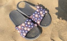 a pair of flip flops with pearls on them sitting in the sand at the beach