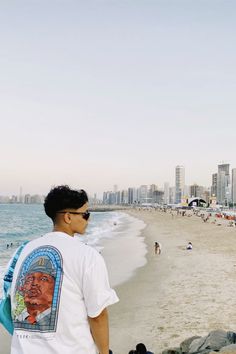 a man standing on top of a sandy beach next to the ocean with buildings in the background