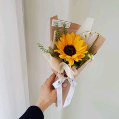 a person holding a bouquet of sunflowers in brown paper wrapped with white ribbon