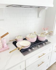 pink pots and pans are sitting on the stove in this white, modern kitchen