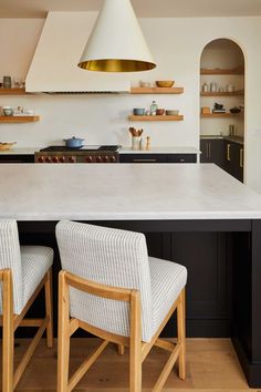 two chairs sitting in front of a kitchen island with an oven and range hood above it