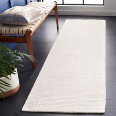 a white rug on the floor in front of a window with a bench and potted plant