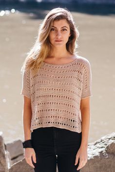 a woman standing next to the water with her hands in her pockets