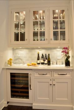 a kitchen with white cabinets and wine bottles on the counter top, along with glassware