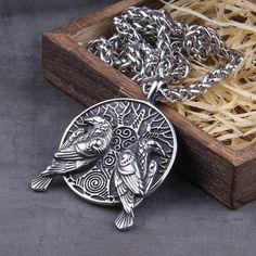 two birds sitting on top of a silver plated necklace in a box with a chain