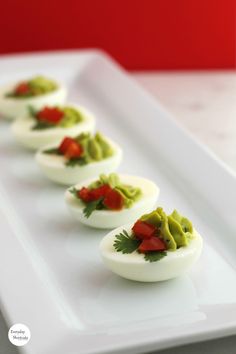 deviled eggs with guacamole and red peppers on a white platter