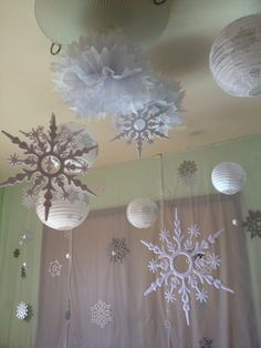 paper snowflakes hanging from the ceiling in front of a curtain with lights on it