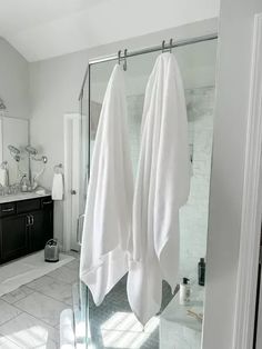 two white towels are hanging on the glass shower door in this modern bathroom with black cabinets and marble flooring