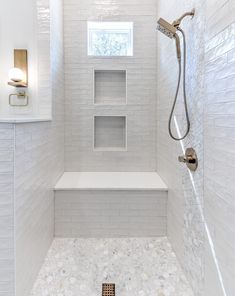 a walk in shower with white tile walls and flooring next to a window on the wall