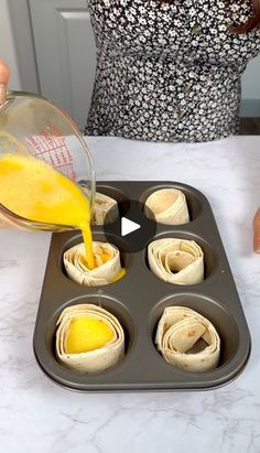 a person pouring orange juice into a muffin tin filled with rolled up pastries