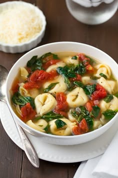 a bowl of pasta and spinach soup on a plate with a spoon next to it