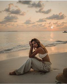 a woman is sitting on the beach at sunset