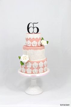 a pink and white wedding cake with flowers on the bottom tier is decorated with black number 65