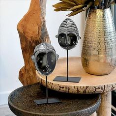 two metal faces are sitting on top of a table next to a vase with flowers