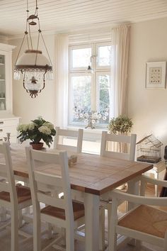 a dining room table and chairs in front of two windows with white trimmings