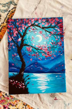 an acrylic painting of a tree by the water with pink flowers on it