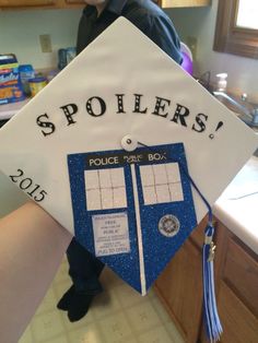 a person wearing a white and blue graduation cap with the words spoilers on it