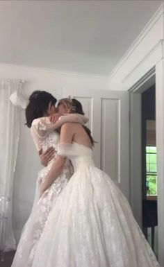 two women in wedding gowns hugging each other while standing next to the door way