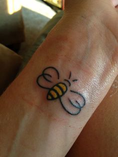 a small tattoo on the wrist of a person with a bee in it's hand