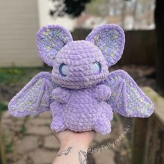 a small purple crocheted stuffed animal with big blue eyes and wings on it's arm