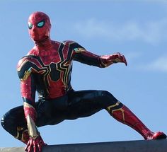 a spider man statue sitting on top of a cement wall in front of a blue sky