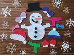 felt snowmen and hats laid out on a wooden floor with snowflakes in the background