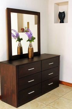 two vases with flowers sit on top of a dresser in front of a mirror