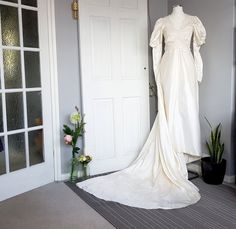 a white wedding dress on display in front of a door with flowers and potted plants