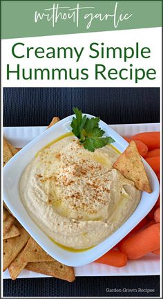 a white plate topped with hummus next to carrots and crackers