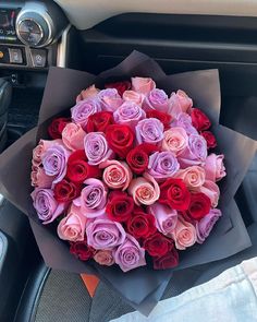 a bouquet of pink and red roses sitting on the dashboard of a car