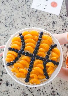 a person holding a plate with oranges and blueberries on it in the shape of an x