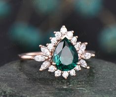 an emerald and diamond ring sitting on top of a rock with diamonds around the band