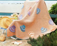 a blanket, hat and seashells on the sand in front of a bench