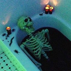 a skeleton sitting in a bathtub with candles on the side and some decorations around it