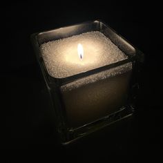 a lit candle in a glass container on a dark surface with water droplets around it