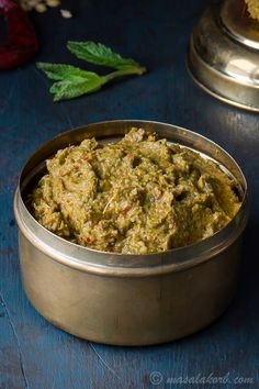 a metal bowl filled with green food on top of a blue table next to other dishes