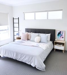 a bed with white sheets and pillows in a bedroom next to two window sills