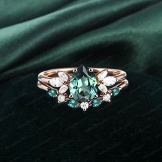 an engagement ring with green and white stones on the side, sitting on top of a velvet