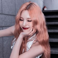 a woman with long red hair posing for a photo in front of a wall and stairs