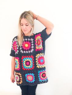 a woman standing in front of a white wall wearing a crochet granny sweater