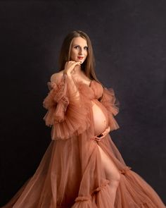 a pregnant woman poses in an orange gown with her hands on her face and one hand under her chin