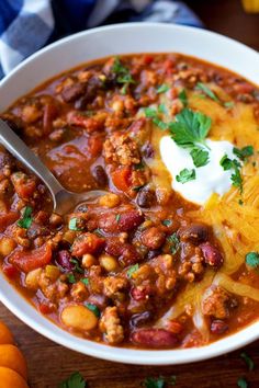 a white bowl filled with chili, beans and sour cream on top of a wooden table