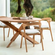 a wooden table with two chairs and a tea pot on top of it next to a tree